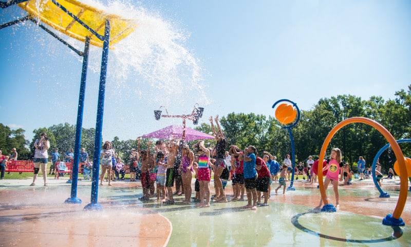 A group of kids playin in the water at the splash pad in Laurel Park.