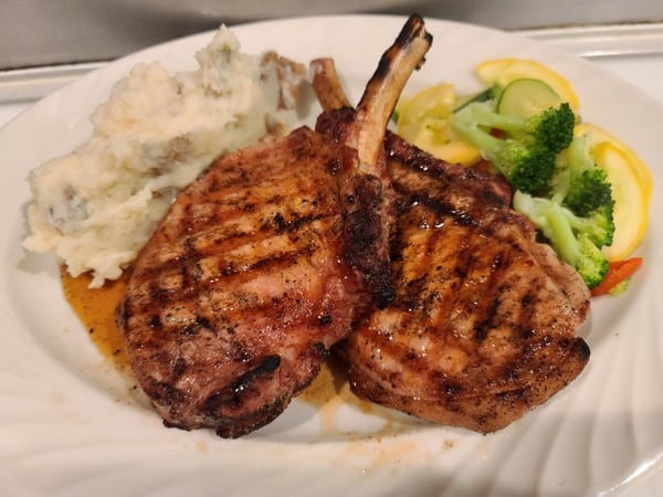 A plate of pork chops, mashed potatoes, and steamed veggies.