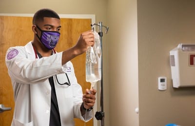 A UCA nursing student hangs IV back in hospital room.
